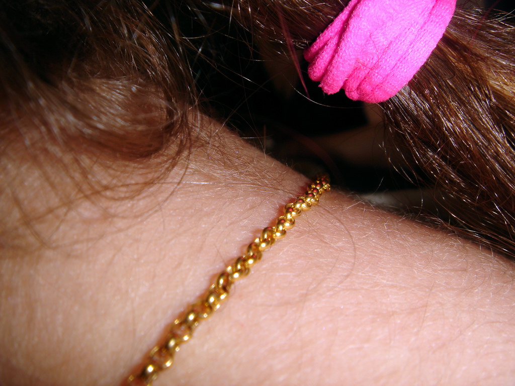 A close up of a neck bearing a gold hair. You can see hair pulled back with a pink tie.